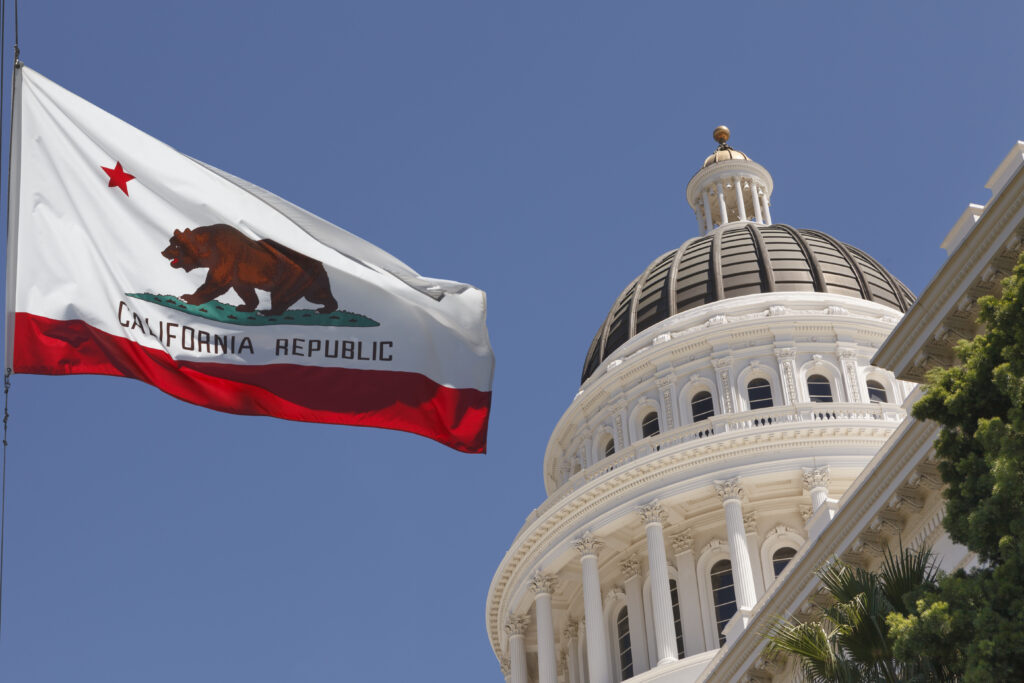 A bright blue sky with the California Capitol Dome and California flag waving in the breeze